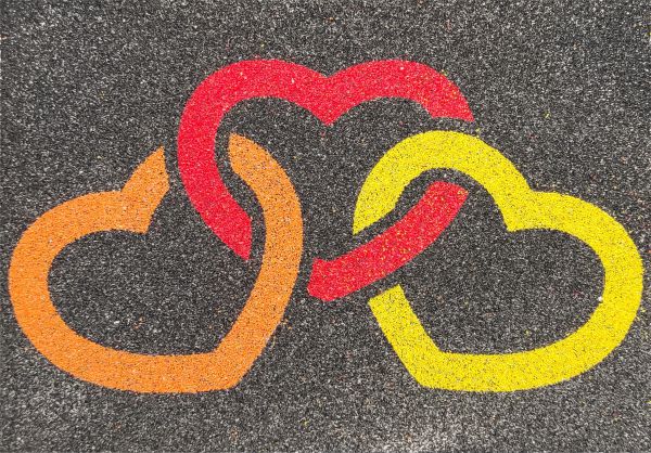 Three heart sand art design with vibrant colors on black background.